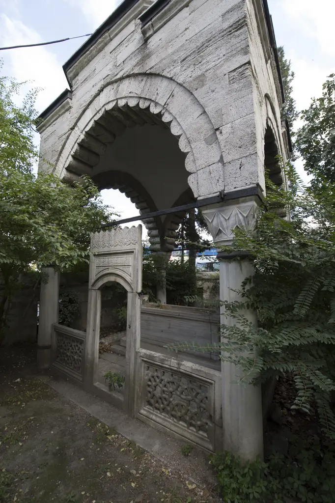 Nazlı Mahmud Çelebi'nin açık türbesi; dilimli taş kemerler, mermer sütunlar, şebekeli korkuluklar ve ağaçlar.