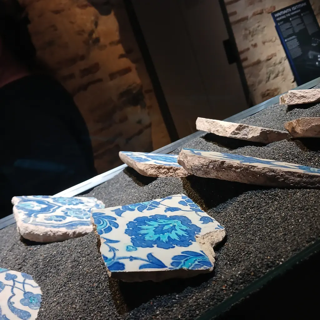 Çinili Hamam Müzesi'nde çini parçaları; çakıl yataklı vitrinde mavi ve firuze palmet desenli kırık İznik parçaları ile mermer kırıkları.