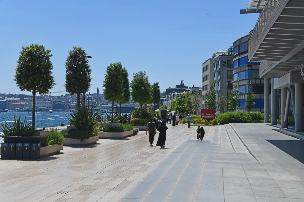 İstanbul Modern'in yanındaki kıyı yolu; saksılarda ağaçlar, taş döşeli rıhtım ve ileride Haliç'in ağzı.
