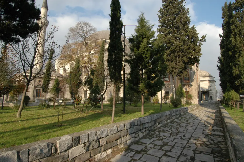Yavuz Sultan Selim Camii'nin haziresi; taş döşeli yol, sıra sıra servi ile çam, sağda türbe cepheleri ve arkada taş istinat duvarı.