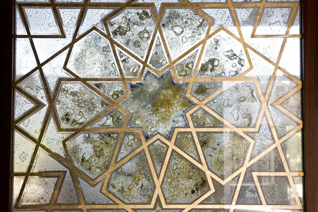 Şakirin Camii'nde pencere; altın renkli çerçeveli yıldızlı geometrik desen, arkasında buzlu cam ve ışık.