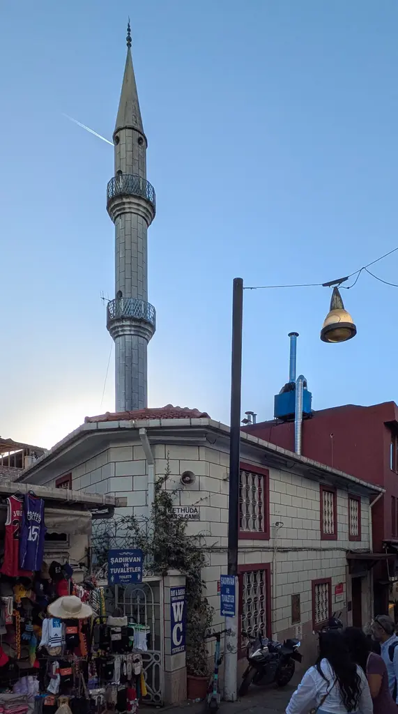 Kadıköy Çarşısı'nda Kethüda Camii; ince taş minare, dükkânların arasında cami cephesi ve sokak lambası.