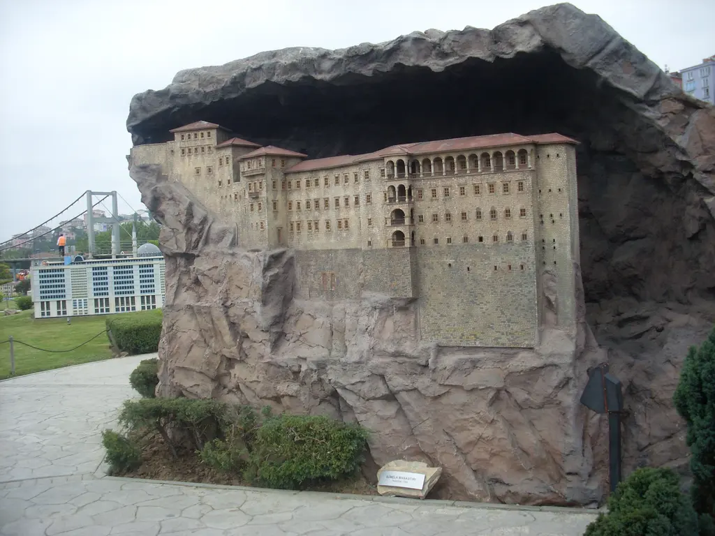 Miniatürk'te Sümela Manastırı maketi; büyük yapay kayanın oyuğuna yerleşmiş krem renkli çok katlı cephe, önde taş yol ve çalılar.