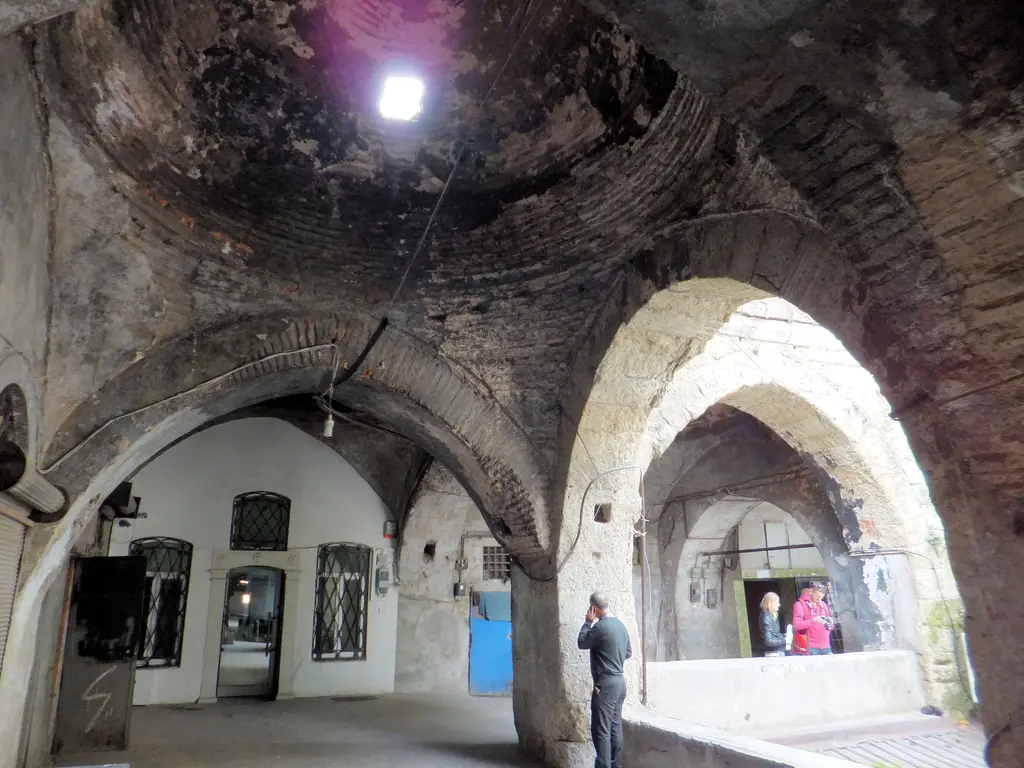 Büyük Valide Han'da üst kat koridoru; üst üste binen tuğla kemerler, sağda kemerli oda kapıları ve koridorun ucunda duran bir kişi.
