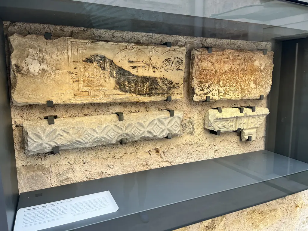 Çinili Hamam Müzesi'nde taş buluntular; cam vitrinde kabartmalı mermer levhalar, hayvan figürü, geometrik bordür ve yazı izleri.