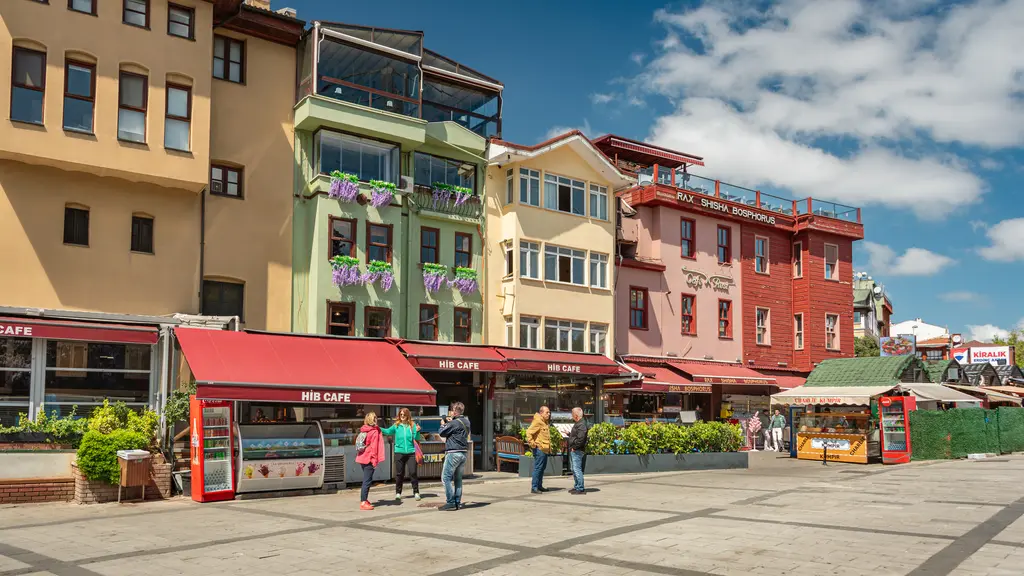 Ortaköy meydanında yan yana renkli evler; sarı, yeşil ve kırmızı cepheler, ahşap cumbalar, tenteler ve taş döşeme.