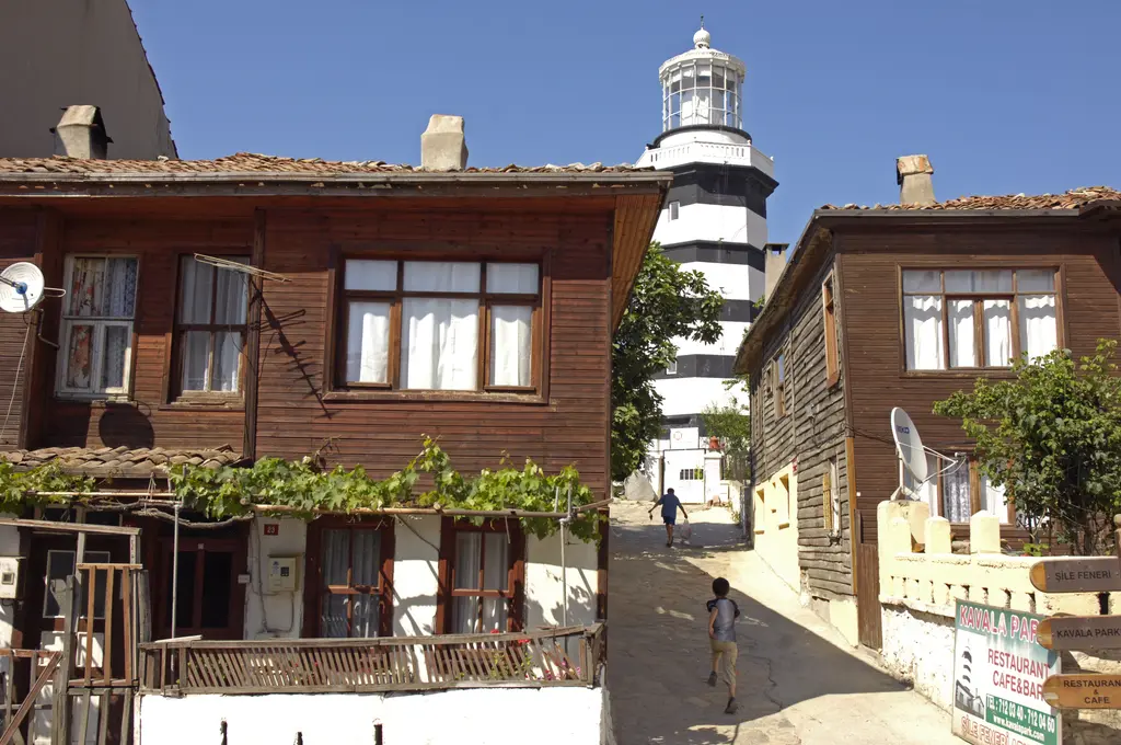 Şile'de ahşap evler; kahverengi ahşap cepheli iki katlı evler, aralarında dar sokak ve arkada Şile Feneri.
