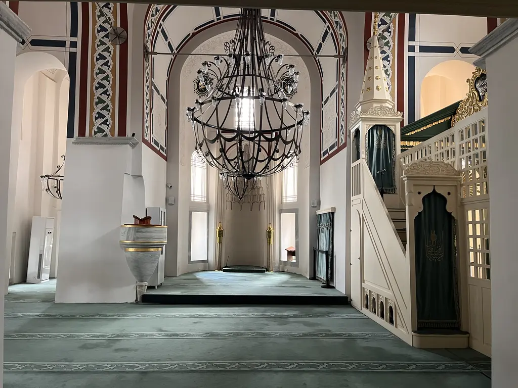 Atik Mustafa Paşa Camii'nin harimi; ortada büyük dövme demir avize, ileride yüksek kemerli mihrap nişi, sağda beyaz ahşap minber, duvarlarda kırmızı lacivert kalem işi bantlar.