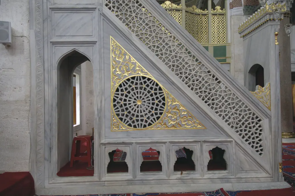 Atik Valide Camii'nin minberi; beyaz mermer korkuluk, yaldızlı şebeke ve oyma geometrik desenler.