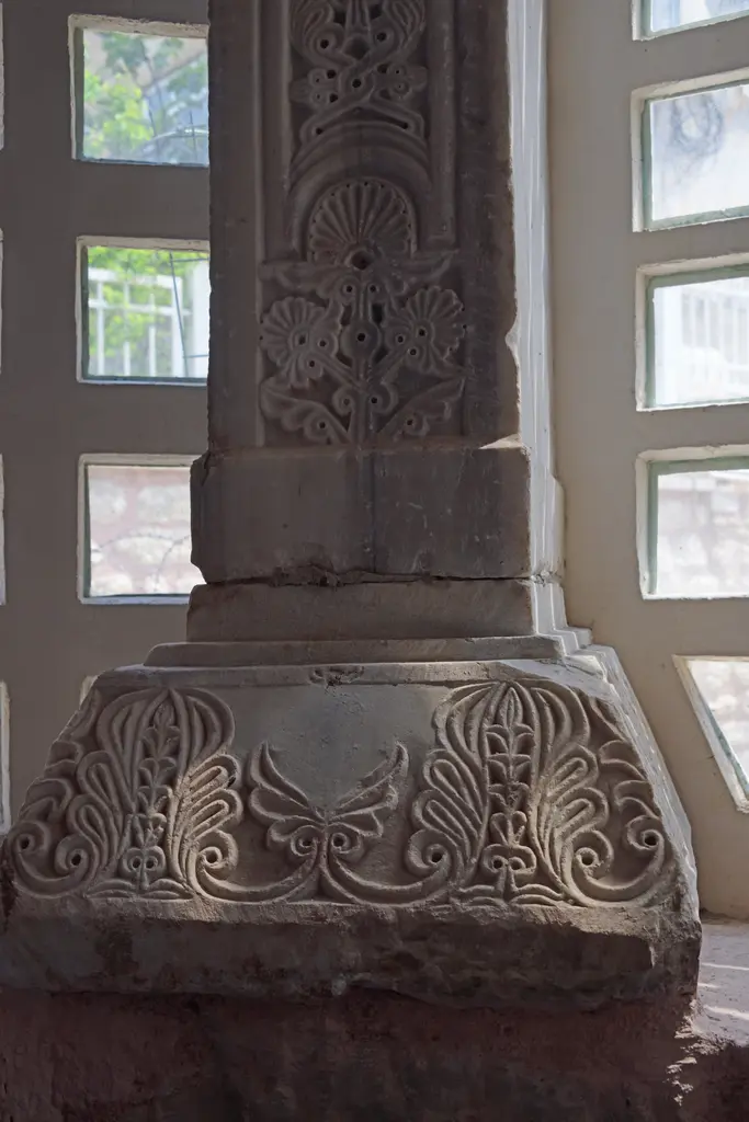 Fenari İsa Camii'nde işlenmiş mermer sütun kaidesi; üç yüzünde simetrik palmet ve rumi bezeme, gövdede ince oyma kuşak, altta çıplak tuğla duvar örgüsü.