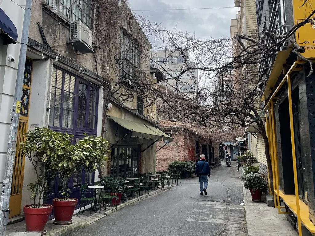 Karaköy'de Ali Paşa Değirmeni Sokağı; saksılı kafe önleri, ahşap ve taş binalar ve sokakta yürüyen bir kişi.