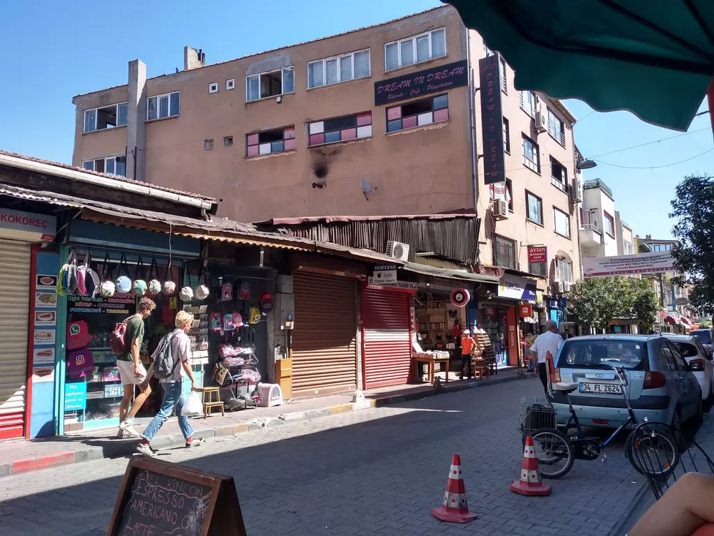 Balat'ta dükkânlı sokak; renkli tabaklar ve hediyelikler sergileyen dükkânlar, park etmiş arabalar ve yayalar.