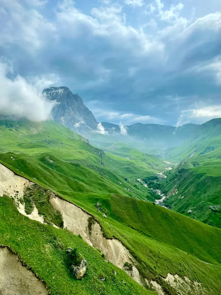 Azerbaycan'ın Qusar bölgesindeki Laza çevresinde yemyeşil dağ vadisi; bulutların sardığı kayalık bir zirve ve vadinin derininde akan dere.
