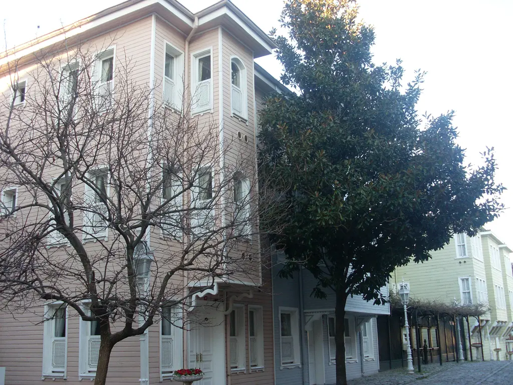 Soğukçeşme Sokağı'nda pembe ve krem boyalı cumbalı ahşap evler; önde yapraksız bir ağaç, yanında yeşil bir ağaç ve taş döşeli yol.