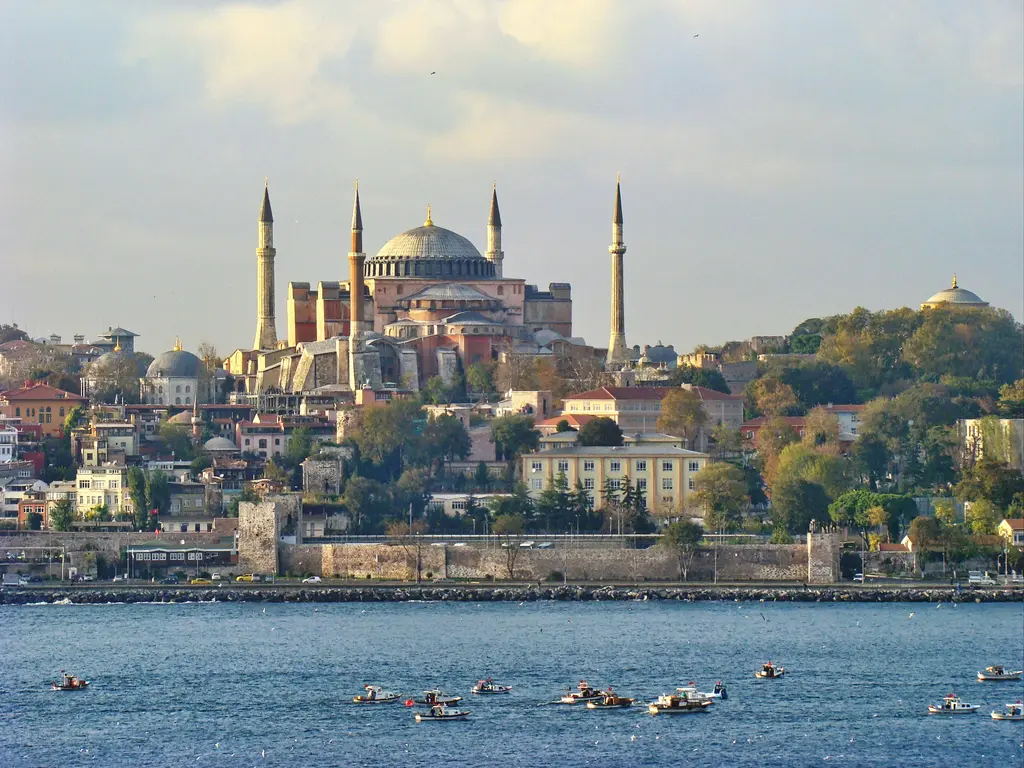 Denizden tarihi yarımada; suda küçük tekneler, kıyıdaki sur duvarı, yamaca yayılan yapılar ve tepede Ayasofya'nın kubbesi ile minareleri.