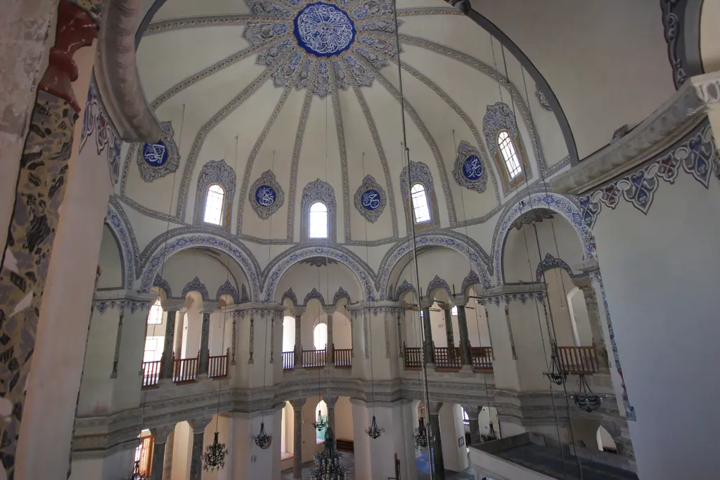 Küçük Ayasofya Camii'nin üst katından harime bakış; kaburgalı kubbe, tepede lacivert göbek, kemerlerde gri mavi bantlar, ahşap parmaklıklı açıklıklar ve benekli mermer sütunlar.
