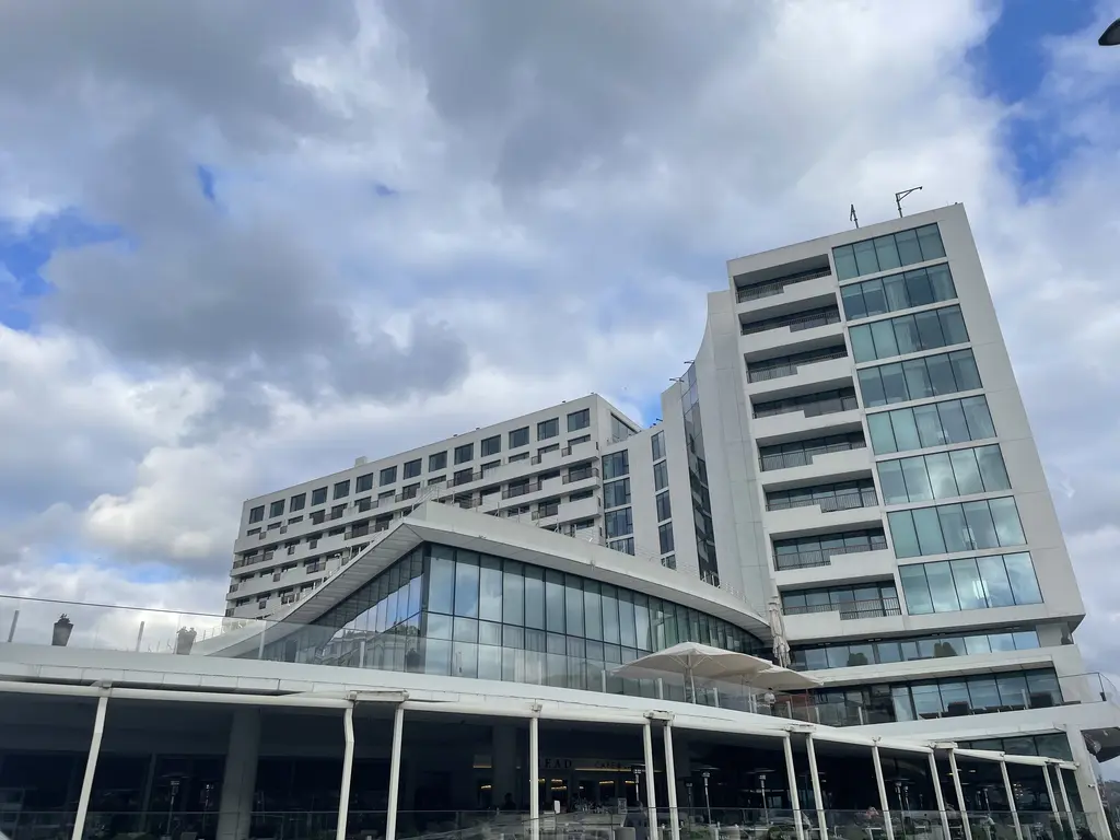 Büyük Tarabya Oteli'nin cam ve beton kanatları; eğimli saçak, cam giriş, yüksek blok ve bulutlu gökyüzü.