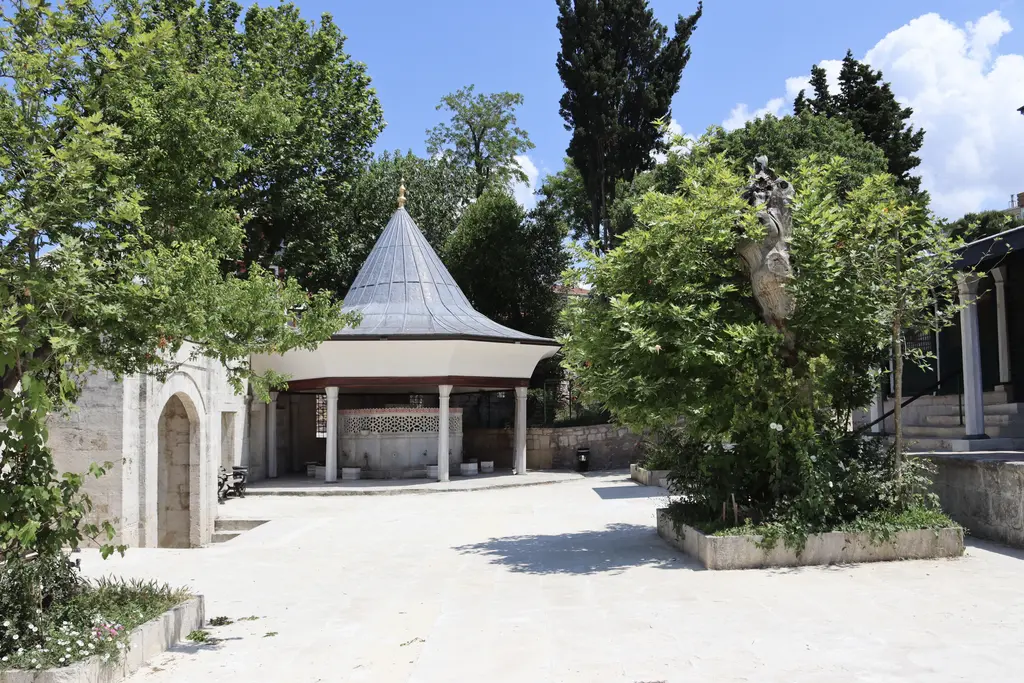 Çinili Camii'nin avlusu; taş zemin, ağaçlar, kurşun külahlı şadırvan ve sağda son cemaat yerine çıkan merdiven.