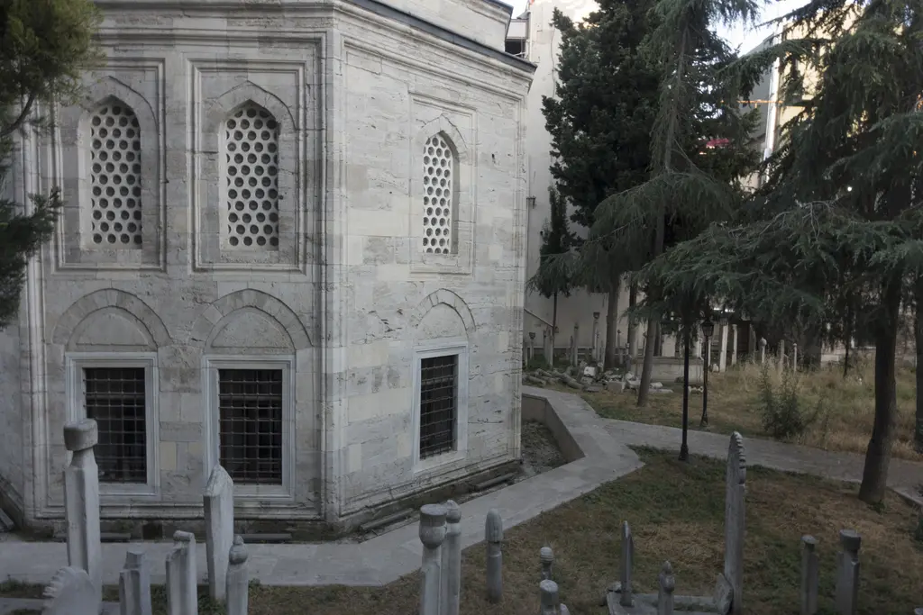 Kılıç Ali Paşa Türbesi; kesme taş cephe, kafesli sivri kemerli pencereler, çevresinde ağaçlar ve hazirenin mezar taşları.