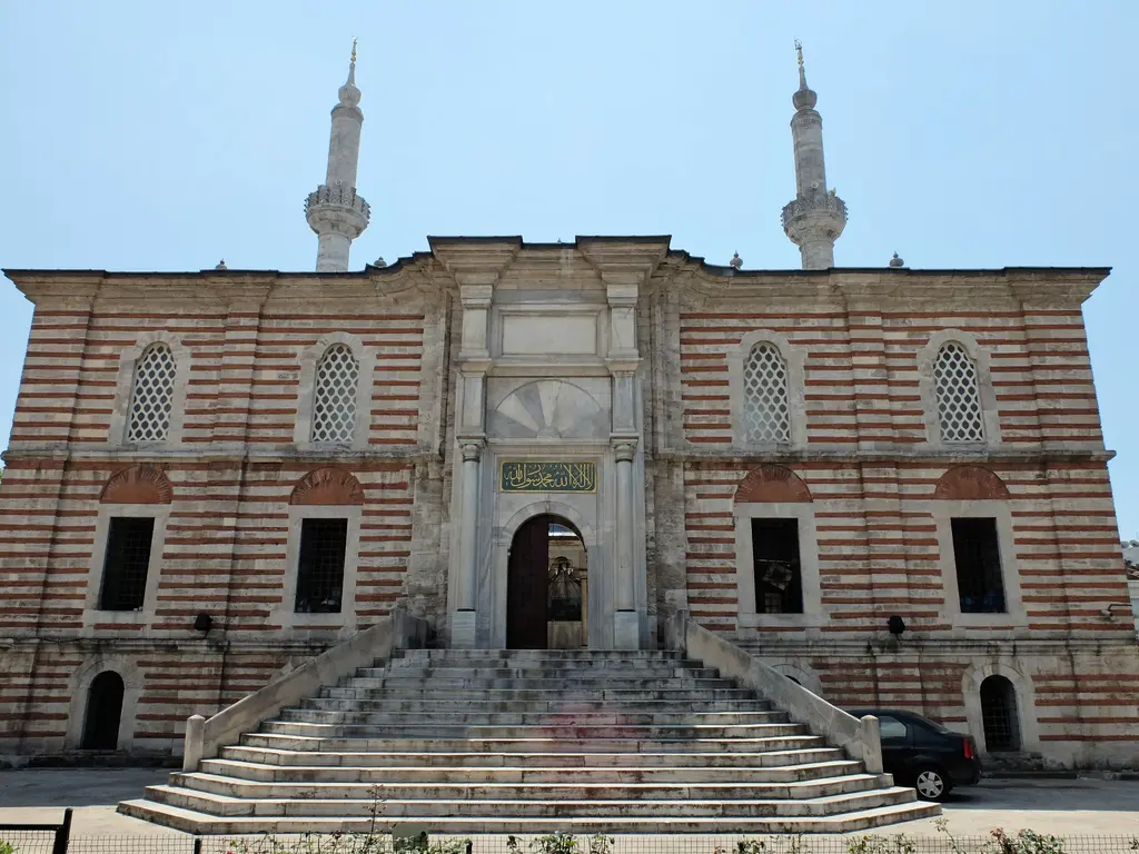 Laleli Camii'nin ön cephesi; taş ve tuğla şeritli duvarlar, iki yanda tek şerefeli minareler ve avluya çıkan geniş taş merdiven.