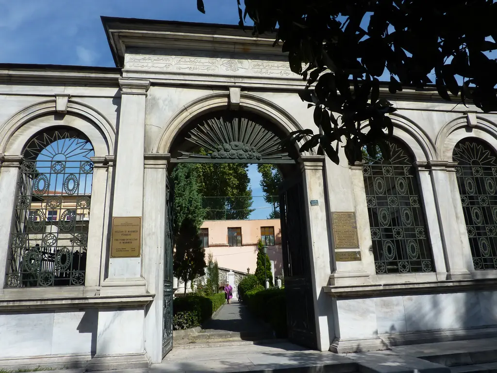 II. Mahmud Türbesi hazire kapısı; mermer çerçeveli yuvarlak kemerli giriş, iki yanda dökme demir şebekeli pencereler, bilgi levhaları ve içeride yeşillik.