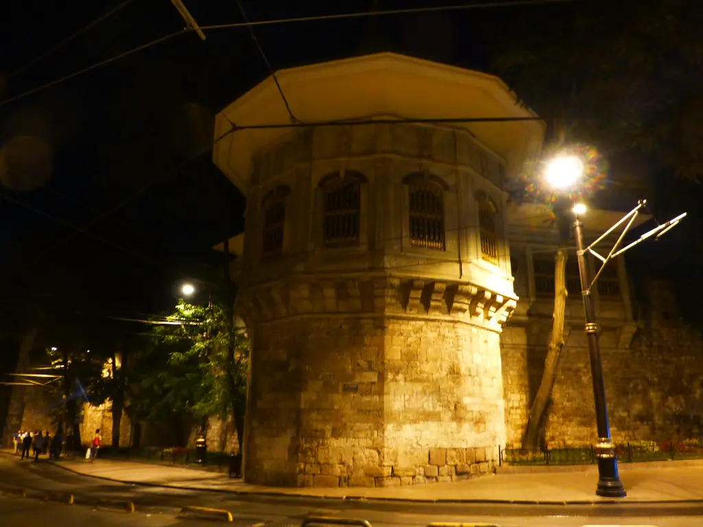 Gece ışıklandırılmış Alay Köşkü; sarı ışıkla aydınlanan taş burç ve mermer salon, önde sokak lambası ve karanlık gök.
