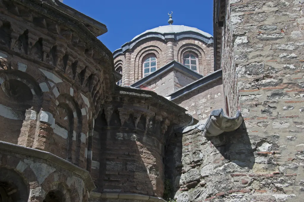Fethiye Camii'nin güneydoğu köşesi yakından; kubbe kasnağındaki ince kemerli pencereler, nişli tuğla duvar ve önde bitişik taş duvar.