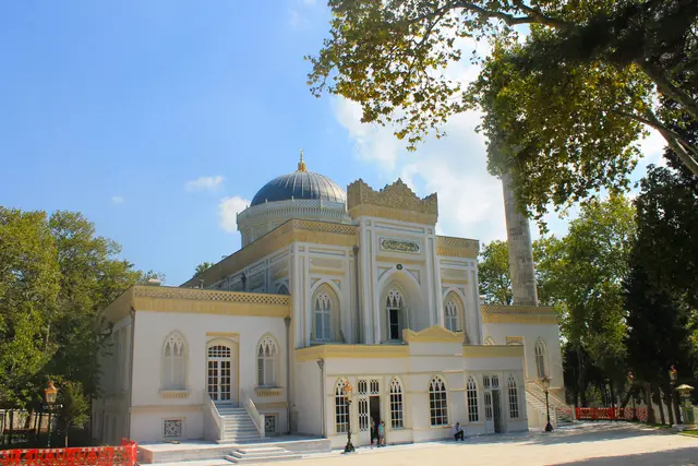 Beşiktaş'ta Yıldız Hamidiye Camii; beyaz ve sarı cephe, mavi kurşun kubbe, sivri kemerli pencereler, ince minare ve çevresinde ağaçlar.