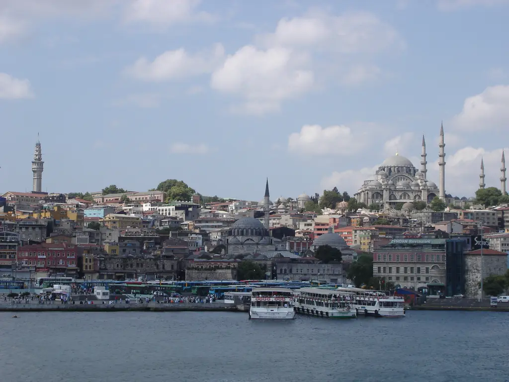 Haliç üstünden Beyazıt Kulesi ile Süleymaniye Camii; suda bağlı tekneler, yamaca yayılan yapılar, kubbeler, minareler ve ince kule.