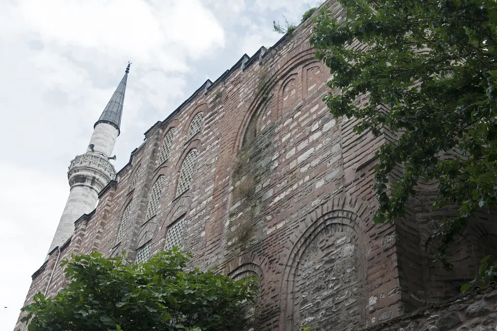 Gül Camii'nin minaresi aşağıdan; korkuluklu şerefe, kurşun külah, yanında güney cephenin kör kemerleri ve altta sarmaşıklı istinat duvarı.