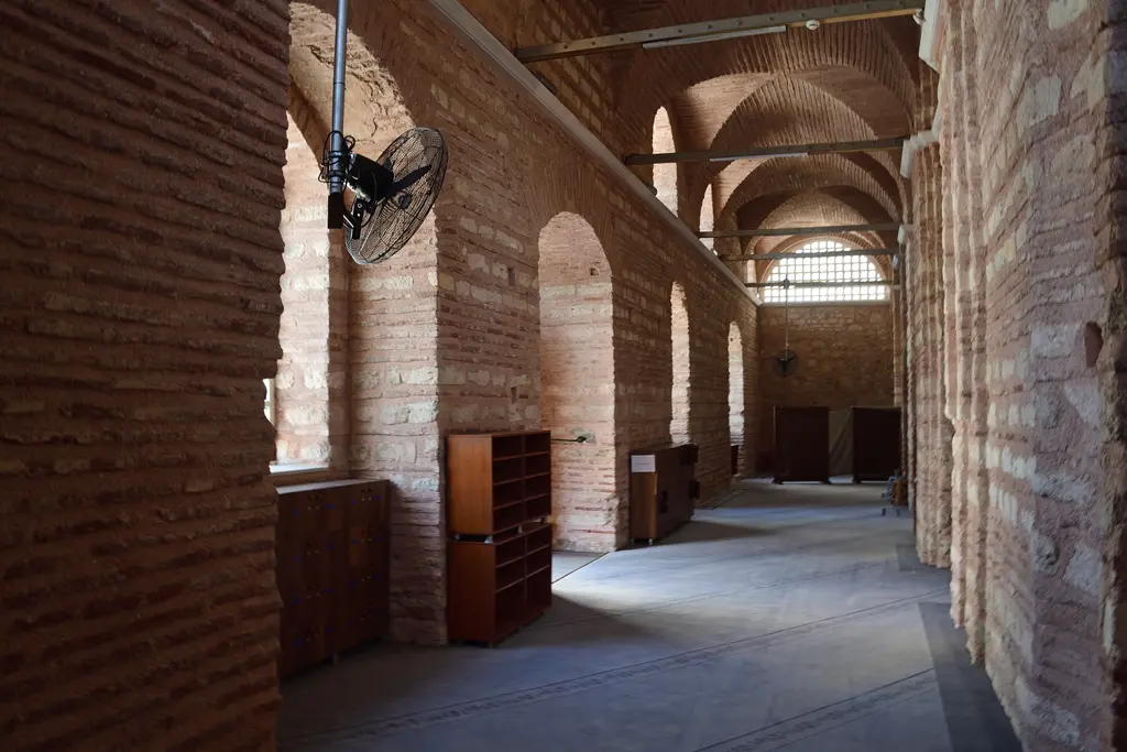 Fenari İsa Camii'nin dış narteksi; sağda tuğla ayaklar ile kemerler dizisi, tavanda beşik tonoz, solda ahşap ayakkabılık dolapları ve gri düz zemin.