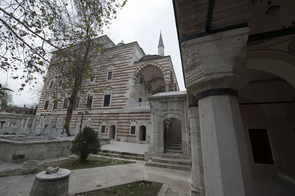 Zal Mahmud Paşa Külliyesi'nin alt bahçesi; caminin yüksek duvarı, kemerli merdiven geçidi, mezar taşları, ağaçlar ve revak sütunu.