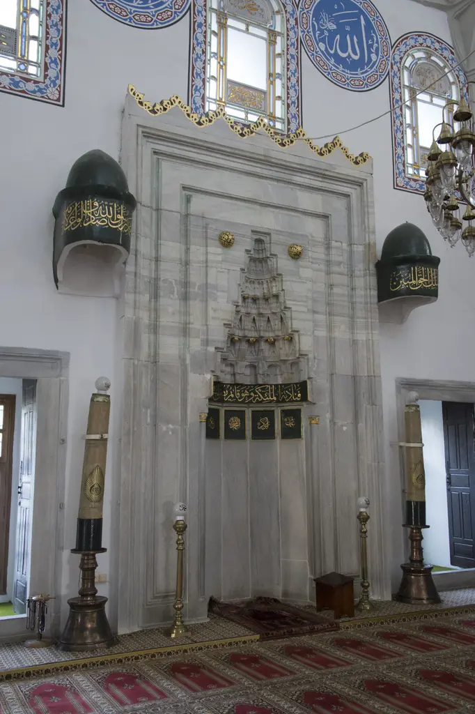 Gazi Atik Ali Paşa Camii'nin mihrabı; mukarnaslı mermer niş, iki yanda yeşil kubbeli mum külahları, şamdanlar ve halı.