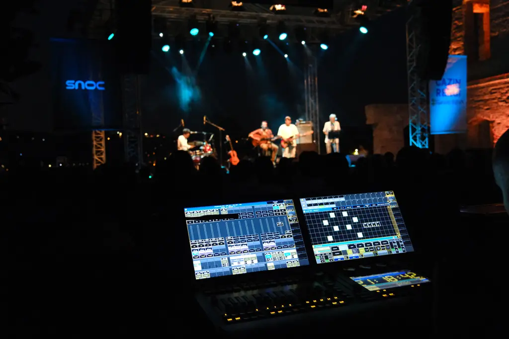 Esma Sultan Yalısı'nda konser; önde ışıklı ses masası, uzakta mavi ışıklı sahnede müzisyenler ve karanlık bahçe.