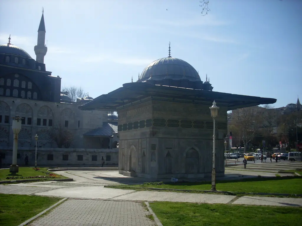 Tophane Meydanı'nda Tophane Çeşmesi; geniş saçaklı kare mermer yapı, çevresinde çimen ve taş yollar, arkada Kılıç Ali Paşa Camii'nin kubbesi ve minaresi.