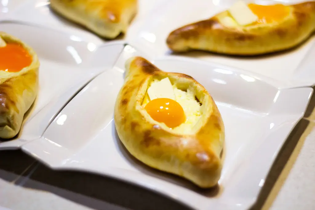 Tabakta yumurtalı, tekne biçimli Acaristan haçapurisi; erimiş peynir ve üstünde tereyağı ile yumurta sarısı.