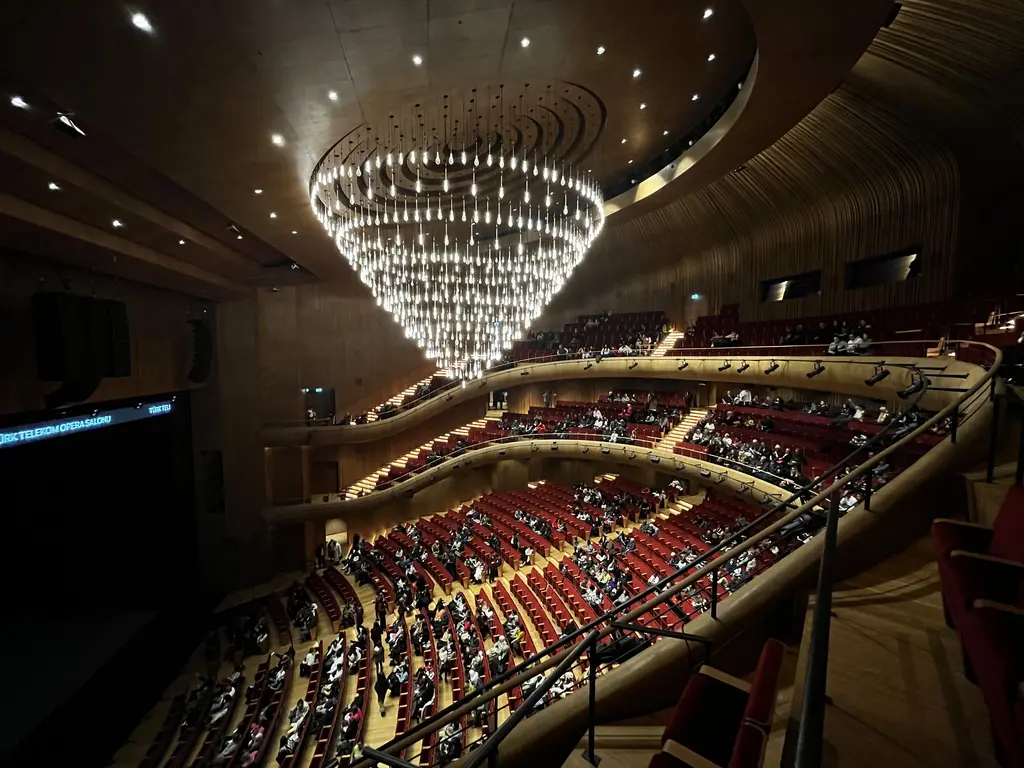 Türk Telekom Opera Salonu; tavandan sarkan büyük kristal avize, kırmızı koltuklar, kıvrımlı ahşap balkonlar ve dolu salon.