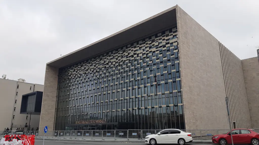 Taksim Meydanı'ndan Atatürk Kültür Merkezi; geniş taş meydan, yürüyen insanlar, bayrak dizileri ve arkada cam cepheli bina.