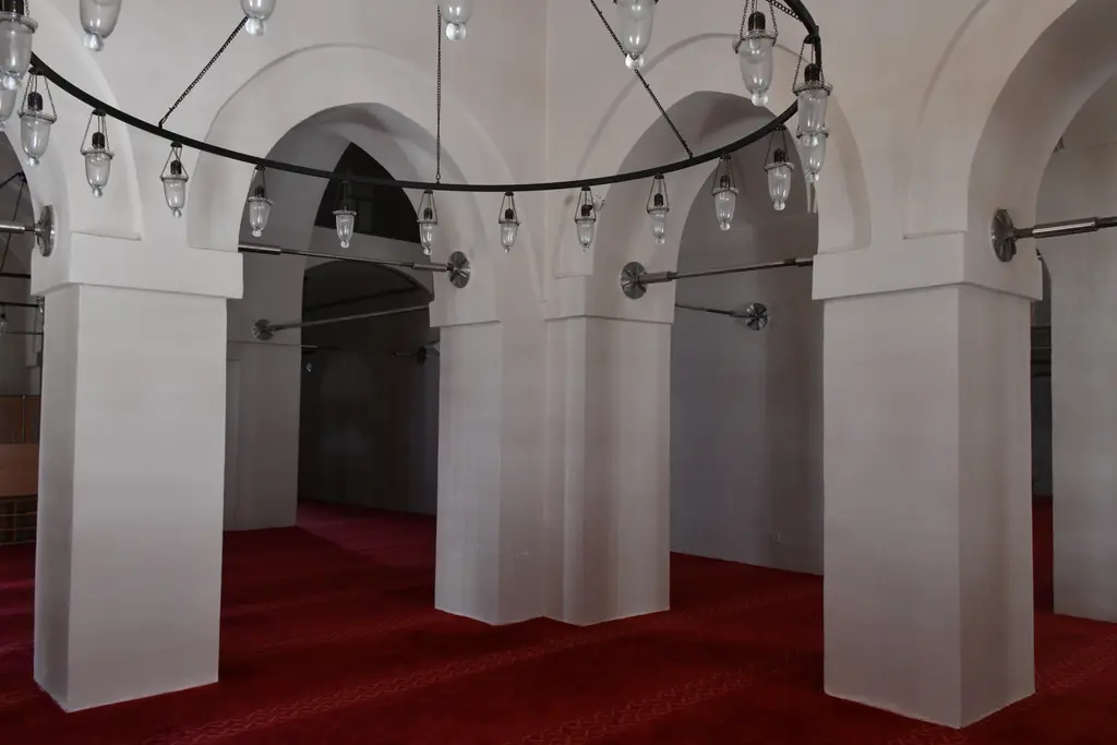 Mahmut Paşa Camii'nin yan mekânı; kalın beyaz payeler, sivri kemerli geçitler, halka avizeler ve kırmızı halı.