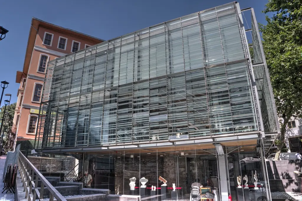 Şerefiye Sarnıcı'nın giriş yapısı; çelik taşıyıcılı camlı çağdaş pavyon, önündeki merdiven ile korkuluk ve arkada mahalle binaları.