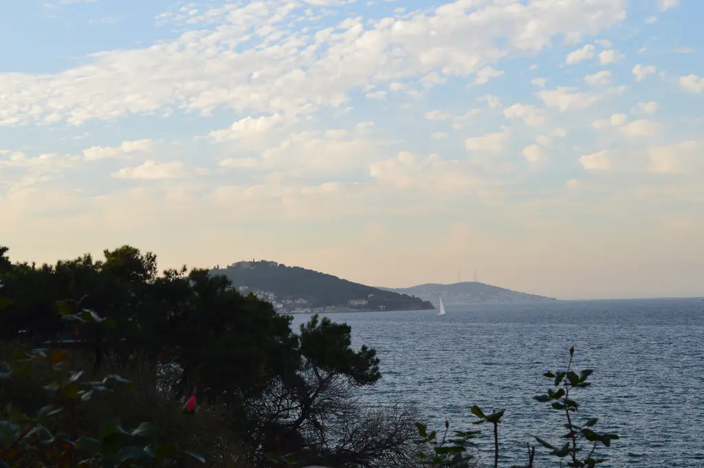 Büyükada'dan Heybeliada; çam ormanlarıyla kaplı ada, kıyıdaki evler ve aradaki mavi deniz.