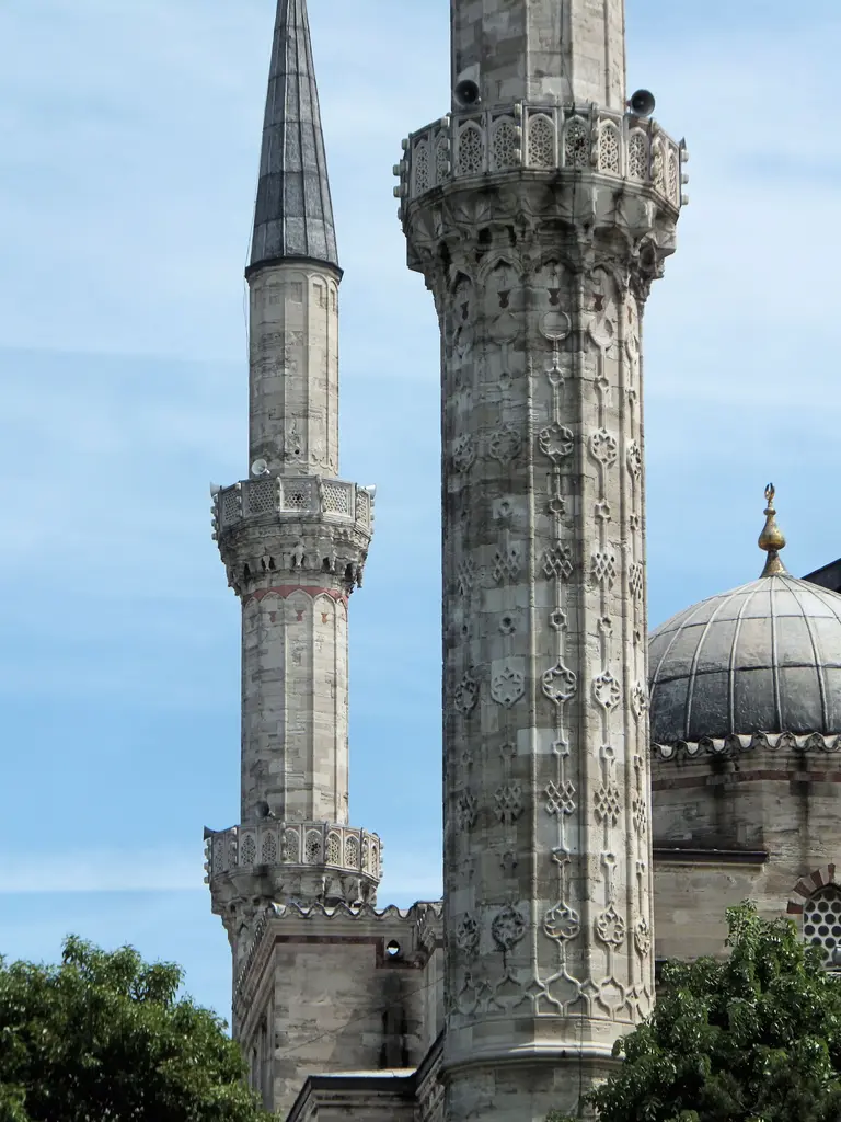 Şehzade Camii'nin iki minaresi yan yana; kabartma bezemeli gövdeler, ikişer şerefe, sağda bir kubbe ile alem, altta ağaç tepeleri ve mavi gökyüzü.