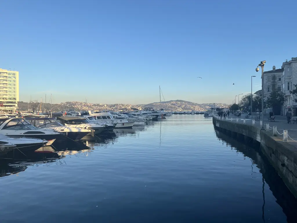 Tarabya Marinası; sakin suda iskeleye bağlı tekneler, sağda taş rıhtım ve sokak lambaları, uzakta koy ağzı.