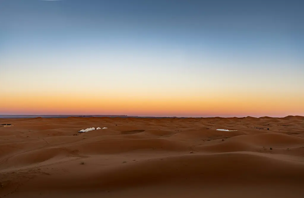 Sahra'da Erg Chebbi kumulları; gün batımı ışığında turuncu kum dalgaları ve keskin kumul sırtları.