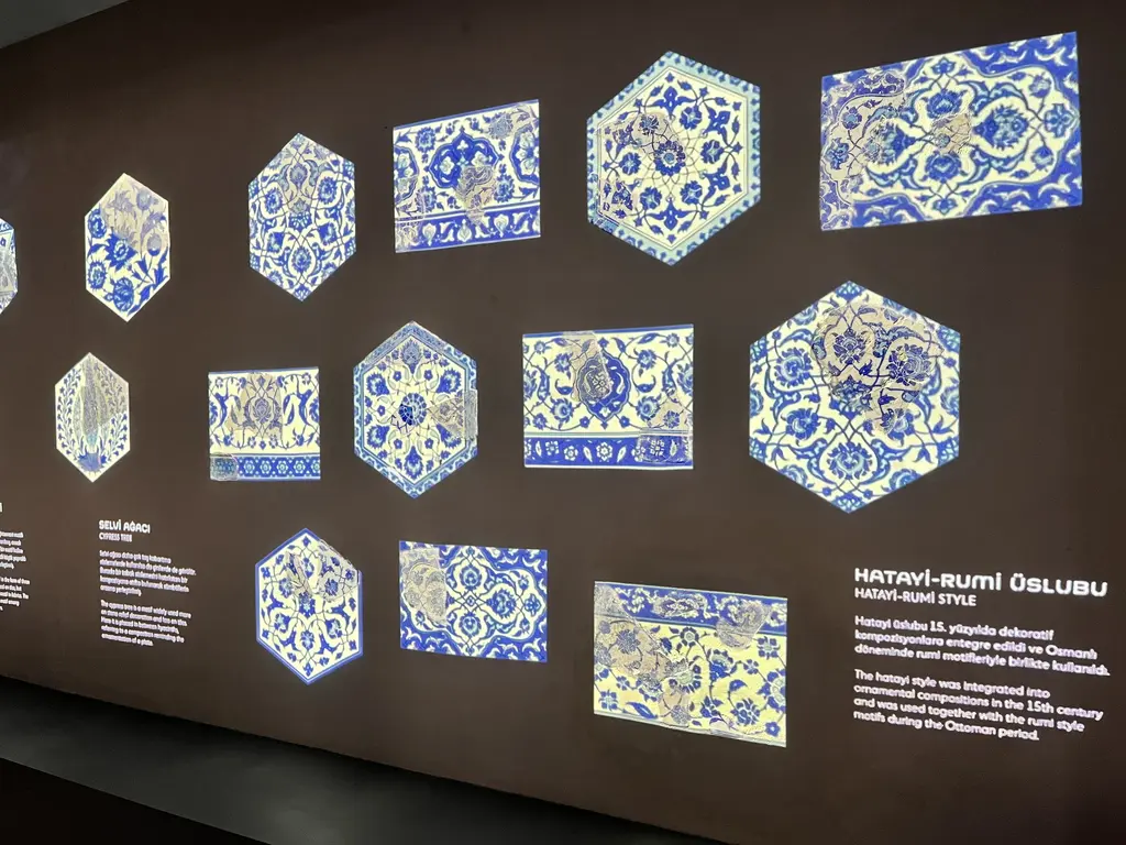 Çinili Hamam Müzesi'nde çini sergisi; koyu duvarda ışıklandırılmış altıgen ve dikdörtgen mavi beyaz İznik çinileri ve üslup açıklaması.