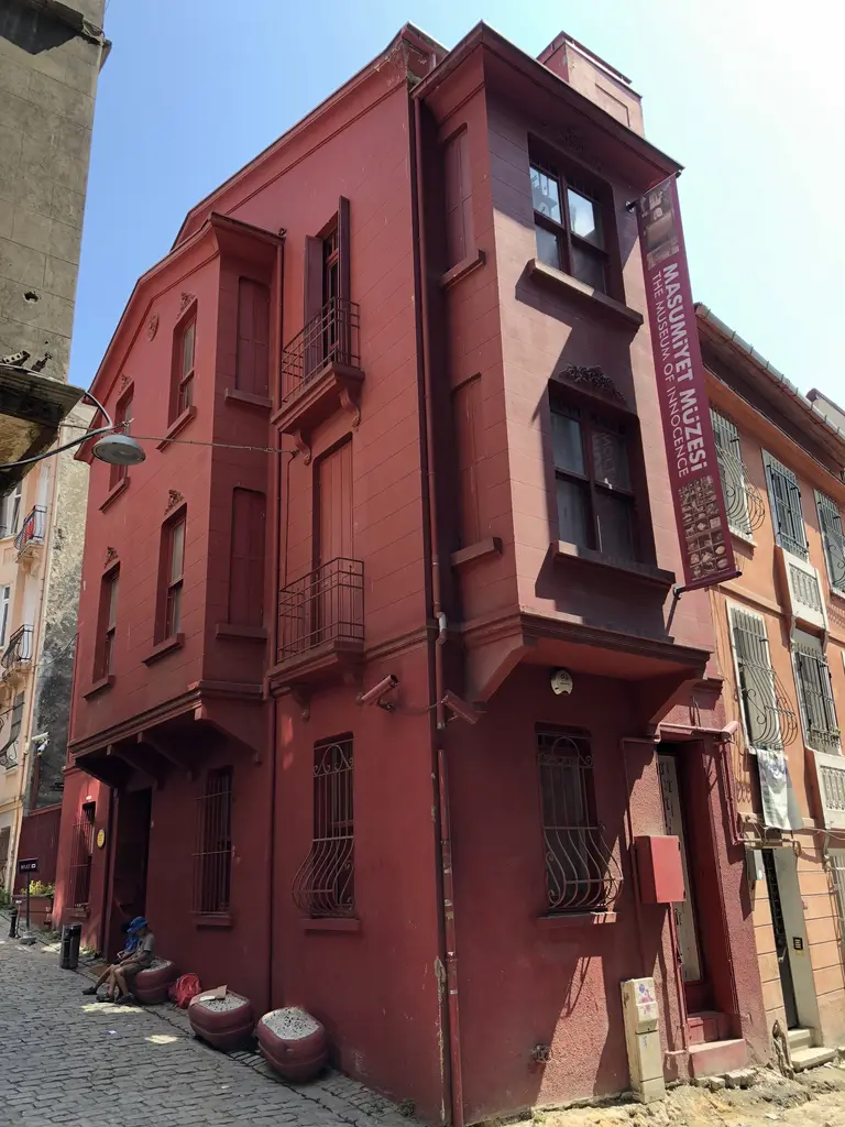 Masumiyet Müzesi'nin sokaktan görünümü; köşedeki kırmızı ev, önünde taş döşeli yol ve yandaki eski binalar.