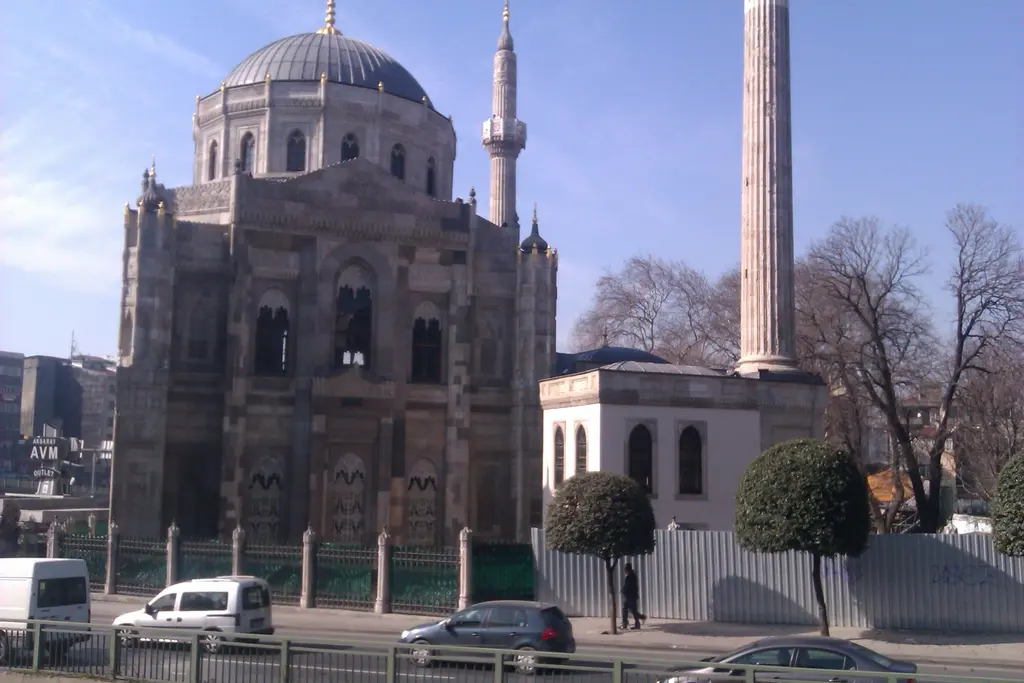 Pertevniyal Valide Sultan Camii'nin yan cephesi; taş gövde, kubbe, minare, sağda beyaz türbe ve önde metal çitli kaldırım.
