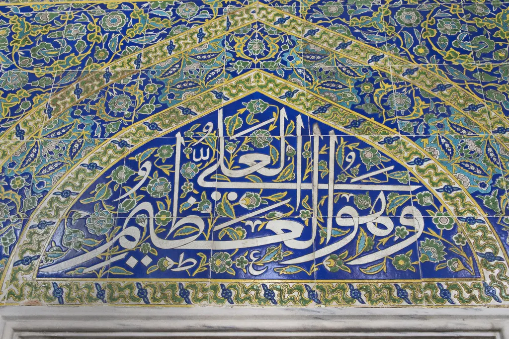 Şehzade Mehmed Türbesi'nde çini alınlık; koyu mavi zemin üzerine beyaz hat yazısı, çevresinde sarı ve yeşil bitkisel kıvrımlar, kenarda bordür şeridi.