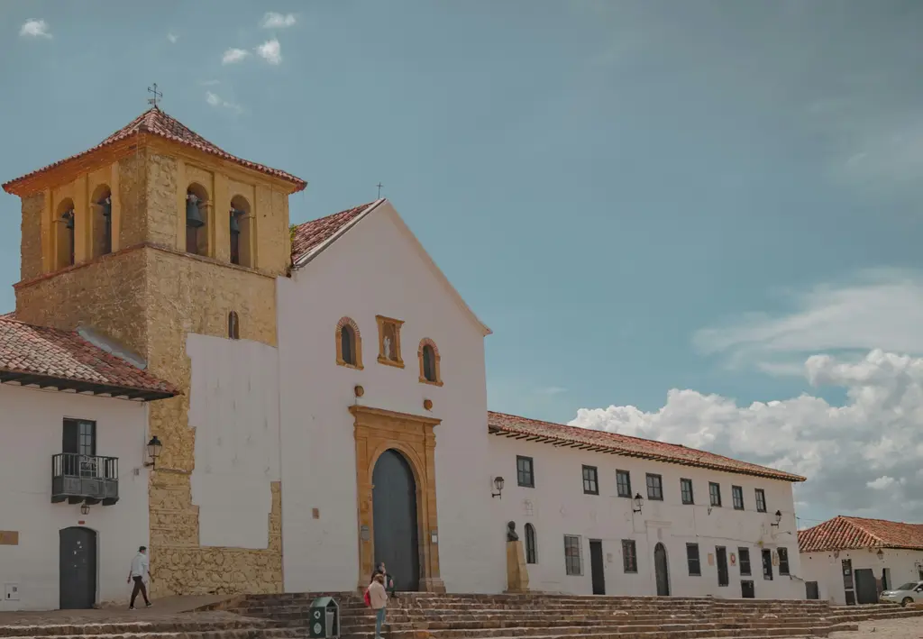Villa de Leyva'da ana meydan; dev taş döşemeli geniş alan, beyaz badanalı sömürge evleri ve arkadaki kuru tepeler.