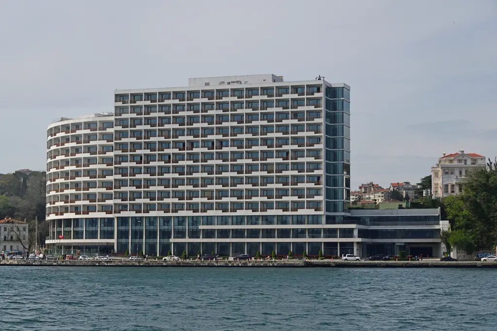 Büyük Tarabya Oteli; suya bakan uzun, beyaz ve balkonlu cephe, alçak giriş katı ve yanında yamaçta yalılar.